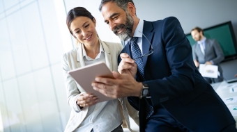 Happy business colleagues in modern office talking and using tablet